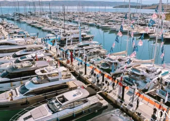 Veduta aerea di un porto affollato di yacht a motore e barche a vela ormeggiati ai pontili, con visitatori e bandierine colorate