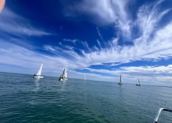 Barche a vela sparse su un mare calmo sotto un cielo azzurro con nuvole sottili e striate
