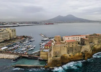 Veduta aerea di Castel dell'Ovo sul mare mosso, con il porticciolo pieno di barche a vela e il Vesuvio sullo sfondo