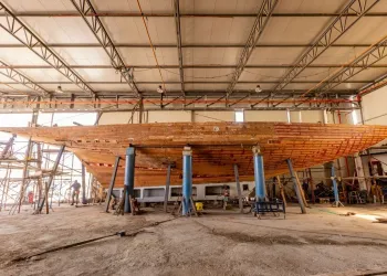 Scafo in legno di uno yacht sostenuto su cavalletti all'interno di un capannone di cantiere