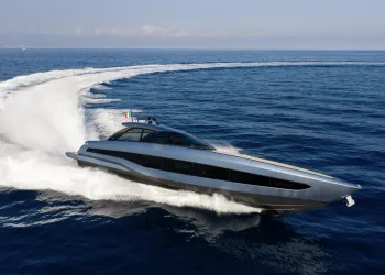 Yacht sportivo dallo scafo grigio metallizzato in alta velocità in mare aperto, con una lunga scia bianca in curva e bandiera italiana a poppa