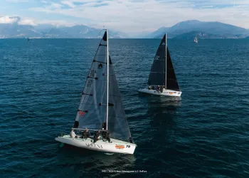 Veduta aerea di due barche a vela con vele scure sul lago, una con scafo bianco e numero 78, con montagne sullo sfondo