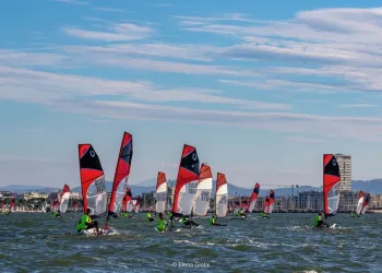 Numerose imbarcazioni con vele rosse e bianche in regata davanti alla costa di Rimini